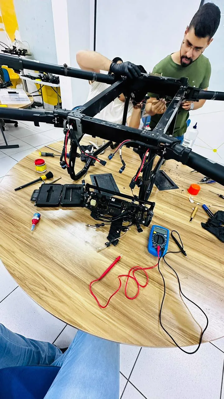 Pessoa de camiseta verde trabalhando na estrutura aberta de um drone agrícola sobre uma bancada.
