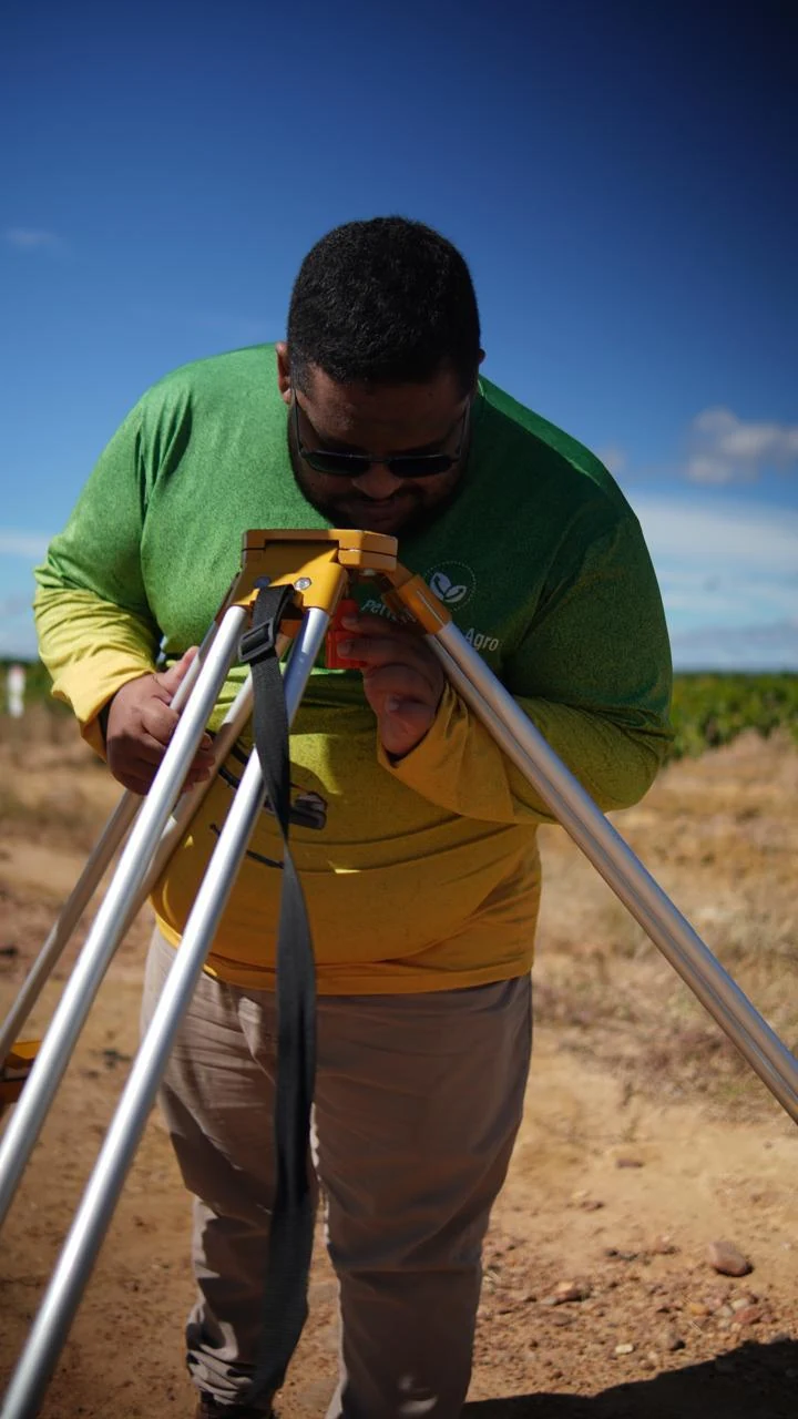 Pessoa utilizando um instrumento de medição sobre tripé em área rural.