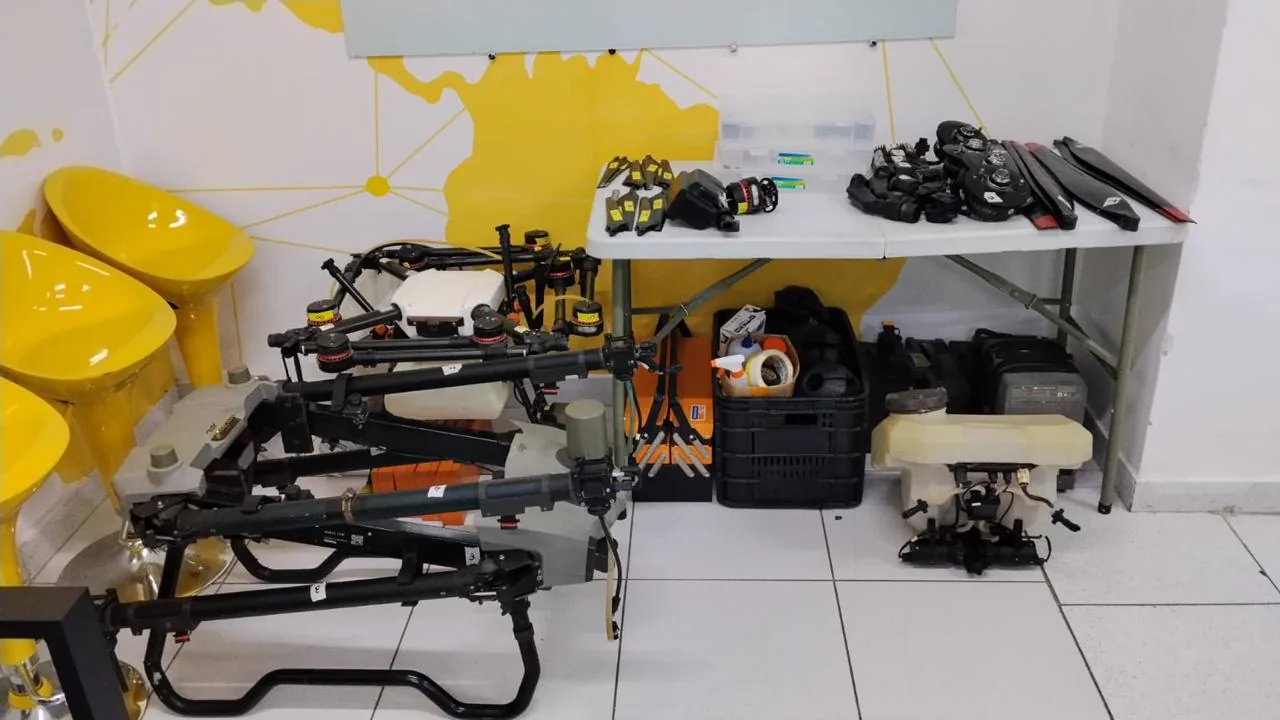 Bancada com drones agrícolas, equipamentos e componentes organizados para atividade técnica.